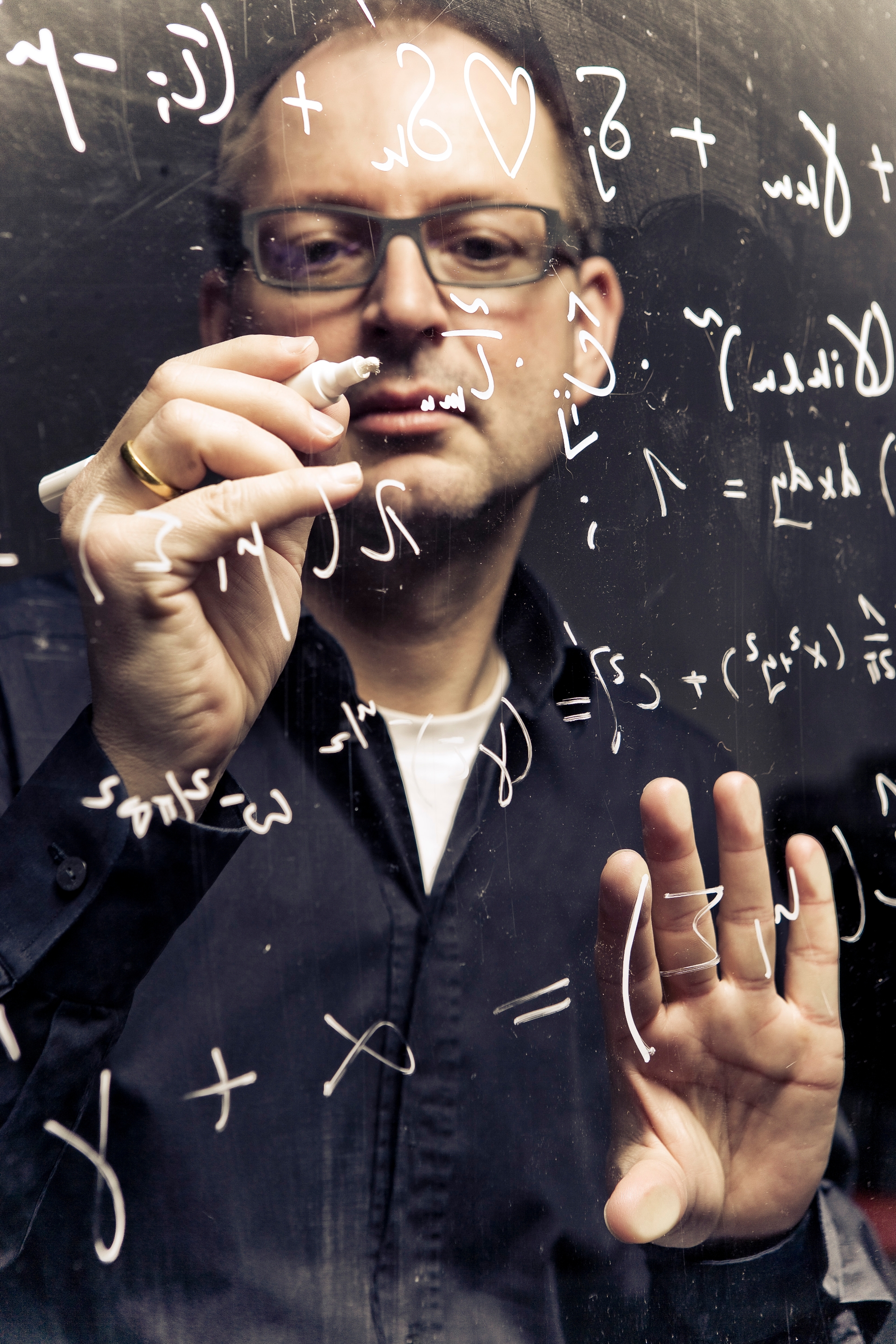 Professor Hesse in front of a glass panel with a white pen in his hand and writing mathematical formulas on it